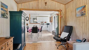 A spacious room with a wooden floor, a dining area with a table and chairs, a black office chair, and a kitchenette in the background.