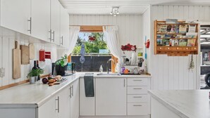 A modern kitchen with white cabinets, a wooden countertop, and a window with a view of greenery.