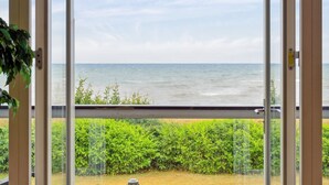 Une vue depuis un balcon avec une porte vitrée, donnant sur une étendue d’eau et un paysage verdoyant.