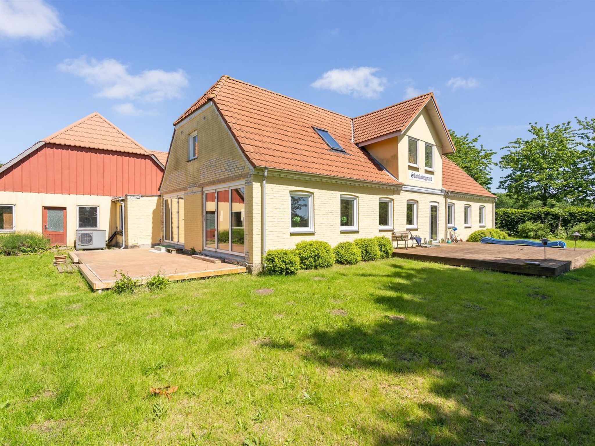 Une maison à deux étages avec un toit rouge, une grande véranda et une piscine.