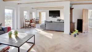 A spacious living room with a wooden ceiling, a grey sofa, a television mounted on the wall, and a small table with flowers. - "Rouwen" - 1km from the sea by Interhome (Sakskøbing)