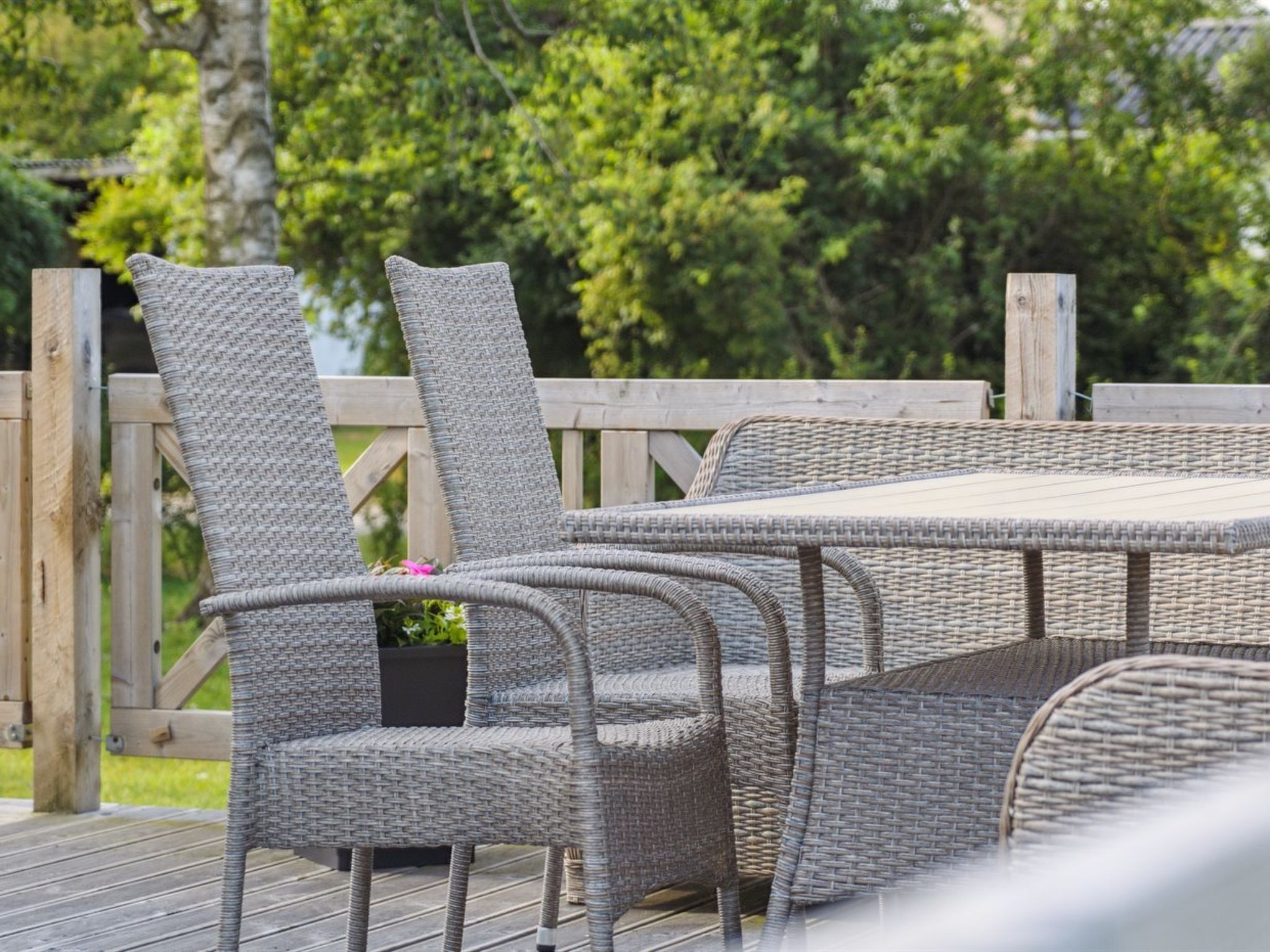 Un ensemble de mobilier de jardin en osier, comprenant une table et des chaises, placé sur une terrasse en bois.