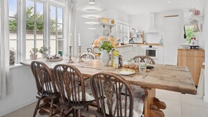 Une cuisine lumineuse avec des meubles blancs, une table à manger en bois et une grande fenêtre.