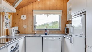 A modern kitchen with wooden walls, stainless steel appliances, and a window with a view of greenery.