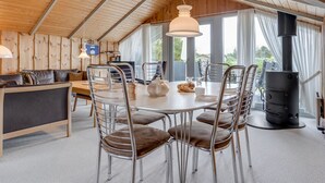 A cozy cabin interior with a dining area, a sofa, and a wood-burning stove.
