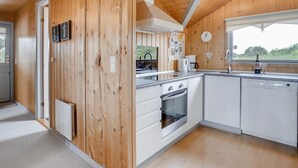 A modern kitchen with wooden walls, white cabinets, a built-in oven, and a window overlooking greenery.