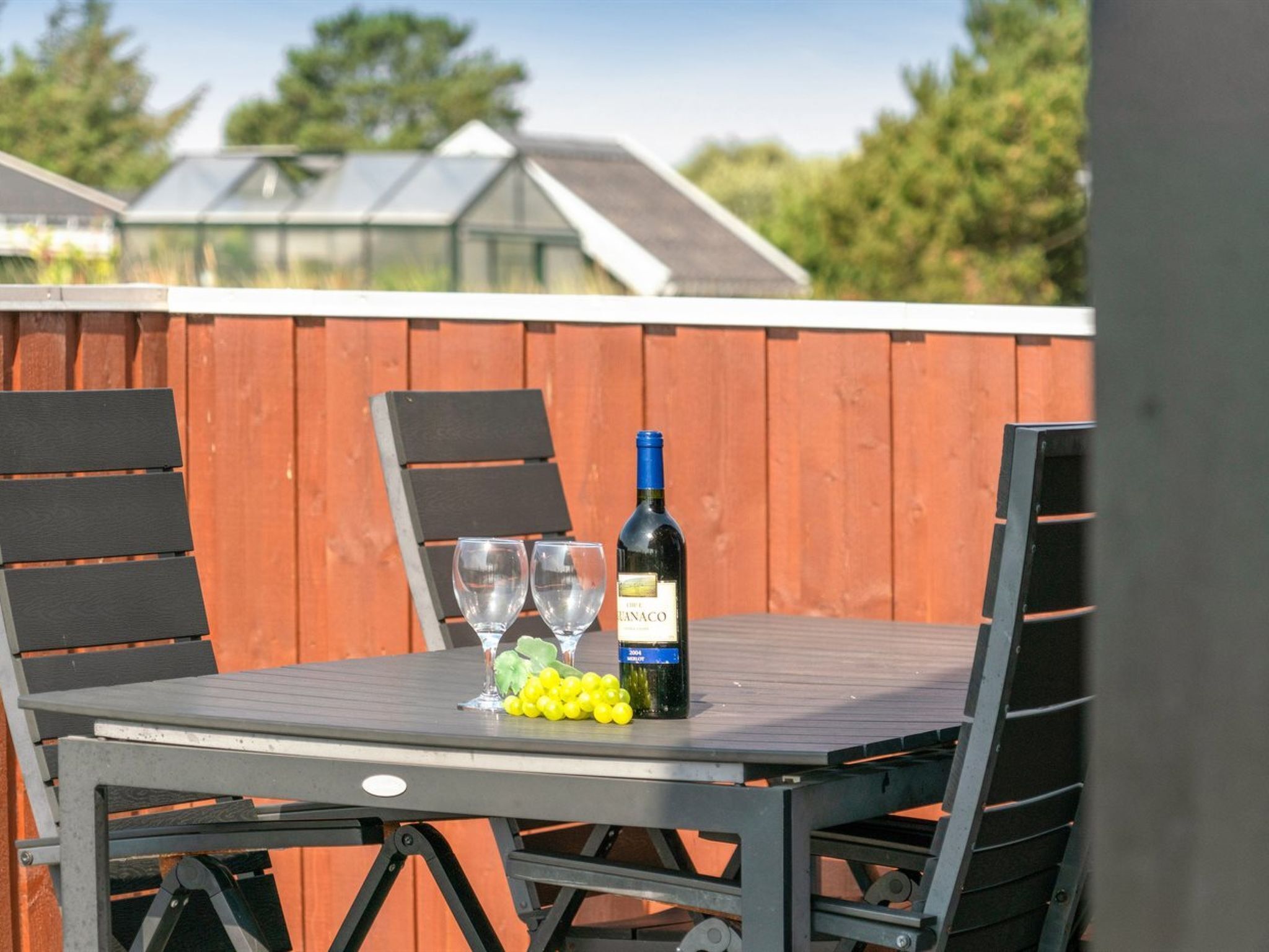 A patio table with two wine glasses, a bottle of wine, and a bunch of grapes.