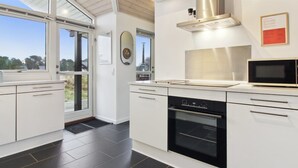 A modern kitchen with white cabinetry, a stainless steel range hood, a built-in oven, and a microwave. - "Tiane" - 800m from the sea by Interhome (Fanø)