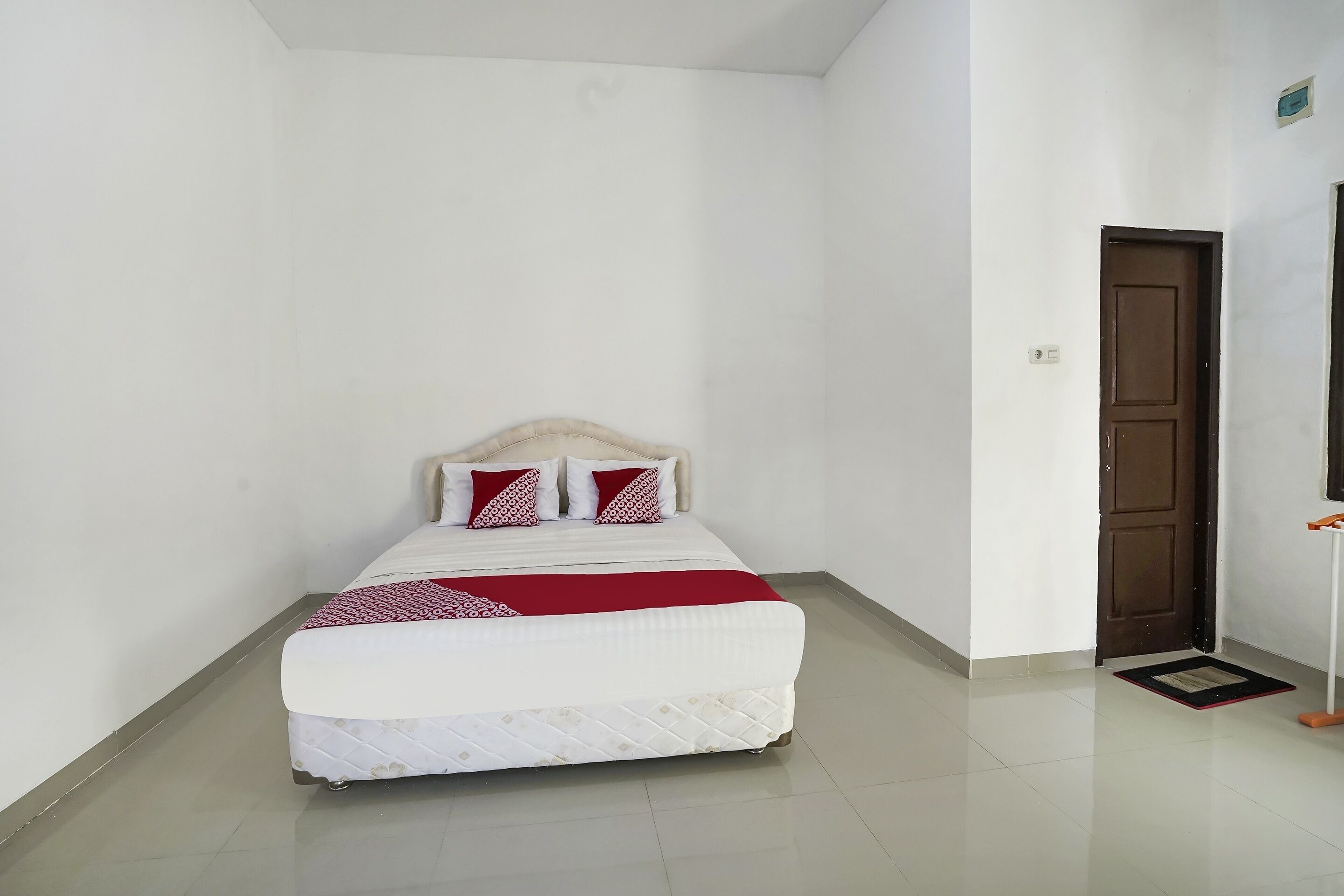 Un lit simple avec une tête de lit, des murs blancs et une porte sur le côté droit.