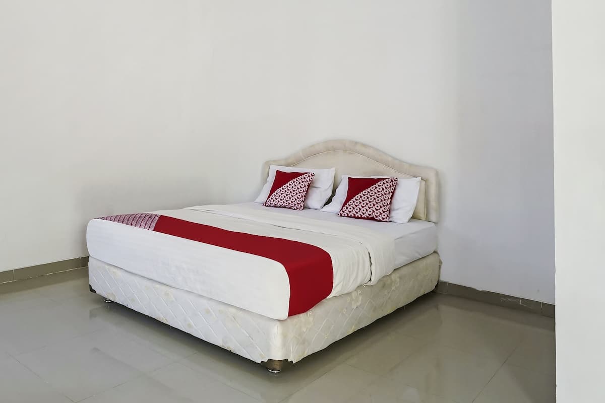 Un lit avec un matelas blanc et une couette rouge, une tête de lit et deux oreillers à motifs rouges et blancs.