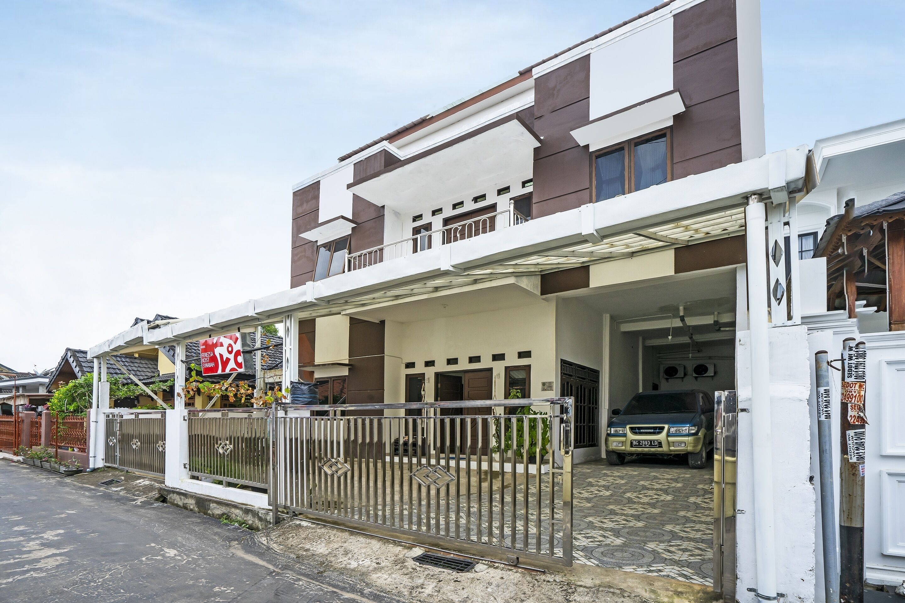 A modern two-story house with a gated entrance, a car parked inside, and a sign indicating a temperature of 27°C.