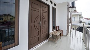 A balcony with a metal railing, a wooden bench, and a large brown door. - OYO 90595 Ferezsa Kost Syariah (Palembang)