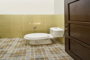 Un baño con inodoro, suelo de baldosas y puerta de madera.