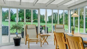 Une véranda avec une table et des chaises, de grandes fenêtres et une vue sur un jardin.