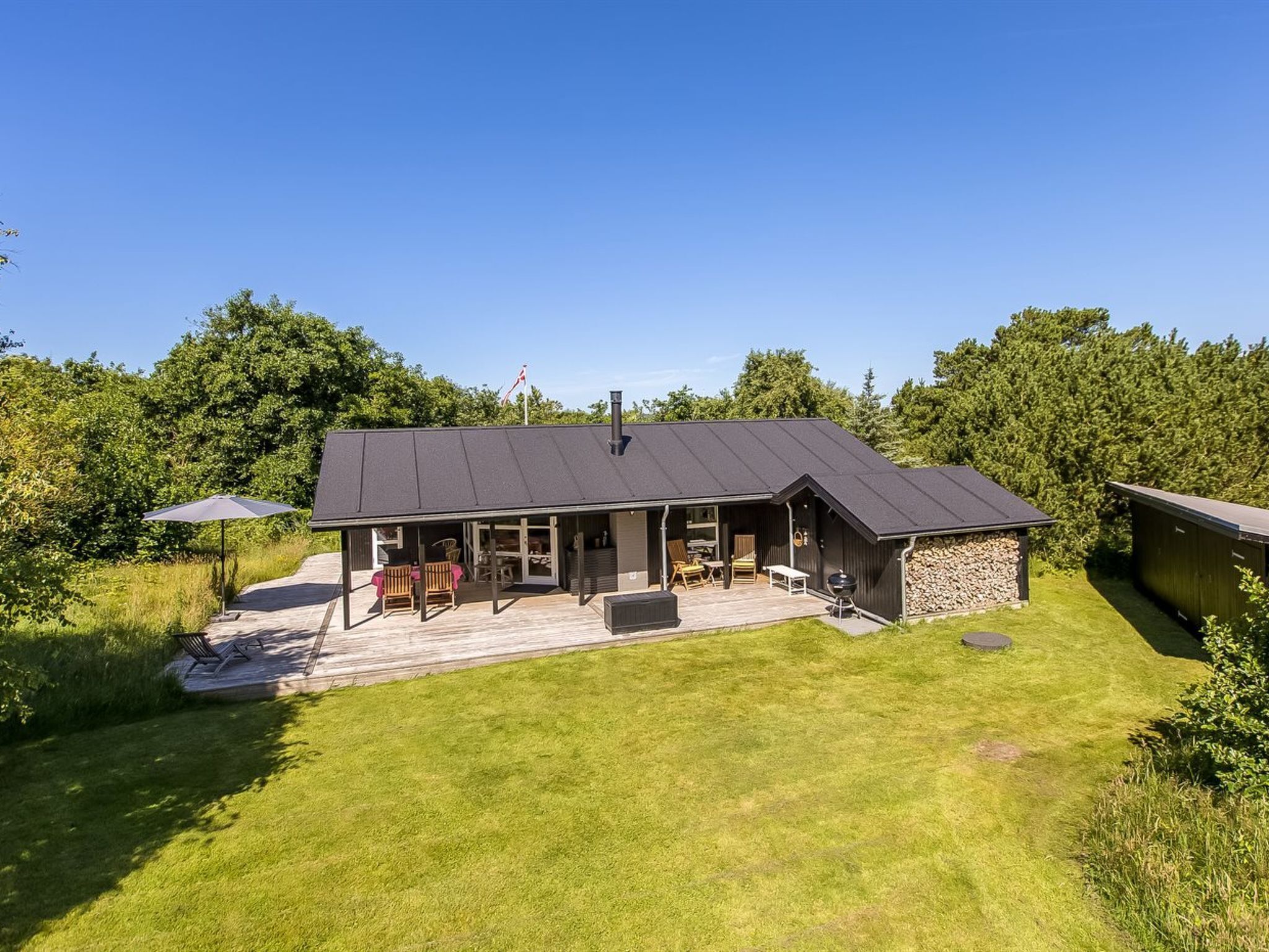Ein modernes Haus mit einer großen Terrasse, einem Grillbereich und einer überdachten Sitzgelegenheit im Freien.