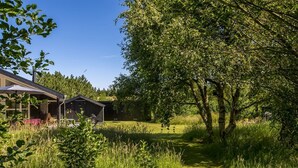 Een rustieke chalet met een overdekt terras, omringd door weelderige begroeiing en een duidelijk pad naar de ingang.