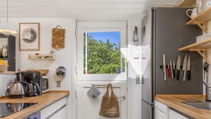 Een compacte keuken met witte kasten, een koffiezetapparaat, een waterkoker en een raam met uitzicht op groen.