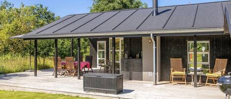 Ett modernt hus med en täckt uteplats, utomhusmöbler och en grill.