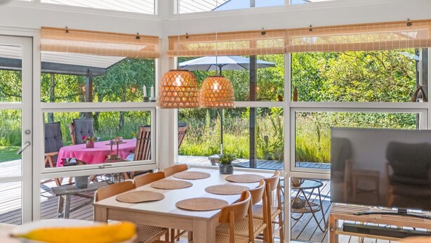 Ruim buitenmeubilair met een grote tafel en stoelen, omgeven door grote ramen met uitzicht op een weelderige tuin.