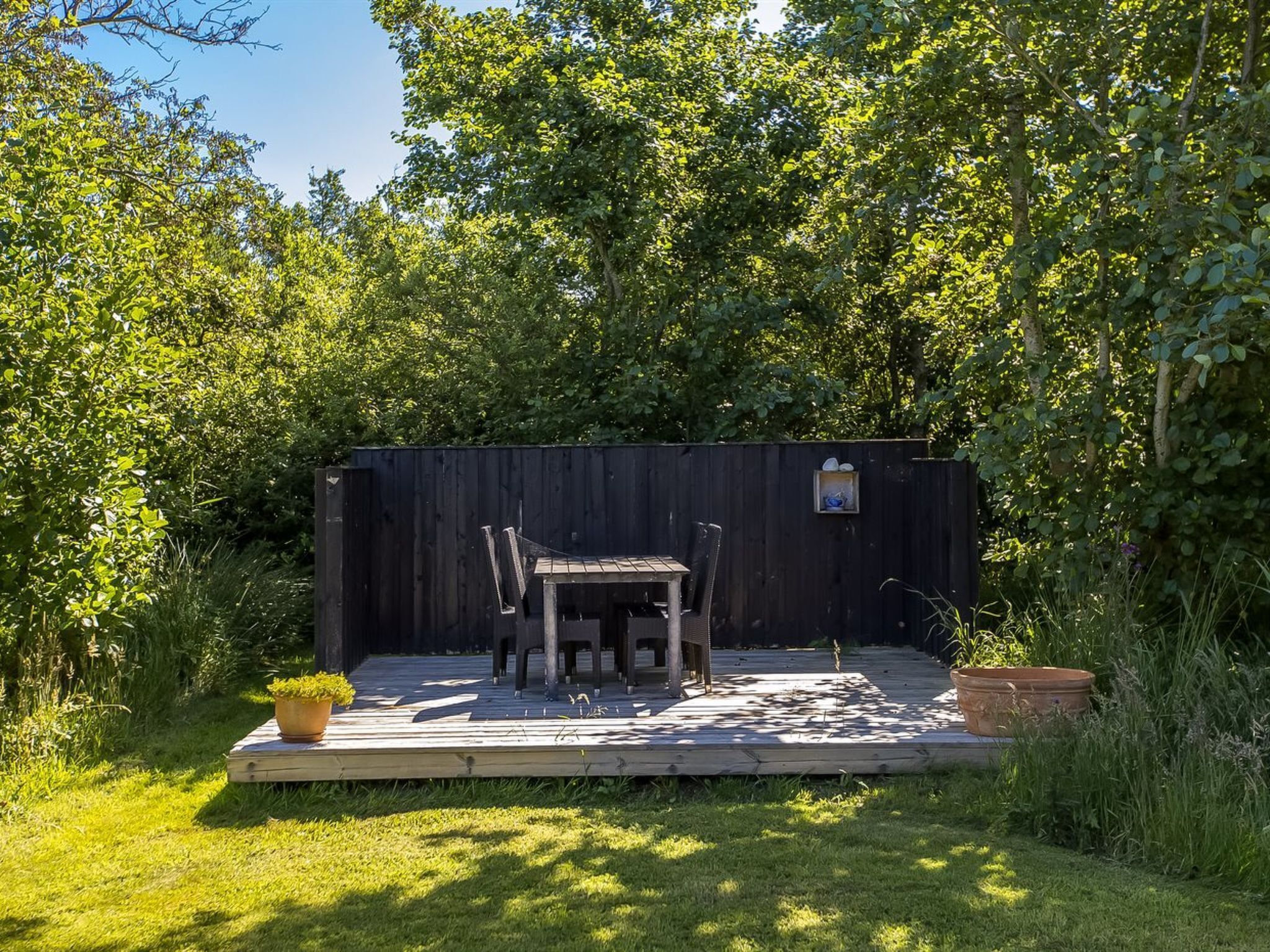 A wooden deck with a table and chairs, surrounded by a wooden fence and lush greenery.