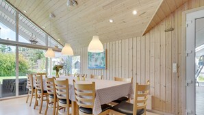 Un comedor con mesa y sillas de madera, ventanas amplias y lámparas colgantes.