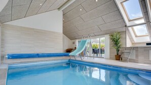 Una piscina interior con tobogán, techo con tragaluces y vistas al exterior a través de amplias ventanas.