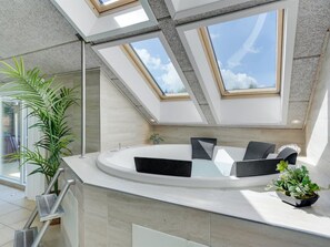 Une salle de bain moderne avec un puits de lumière, une baignoire et une plante en pot.