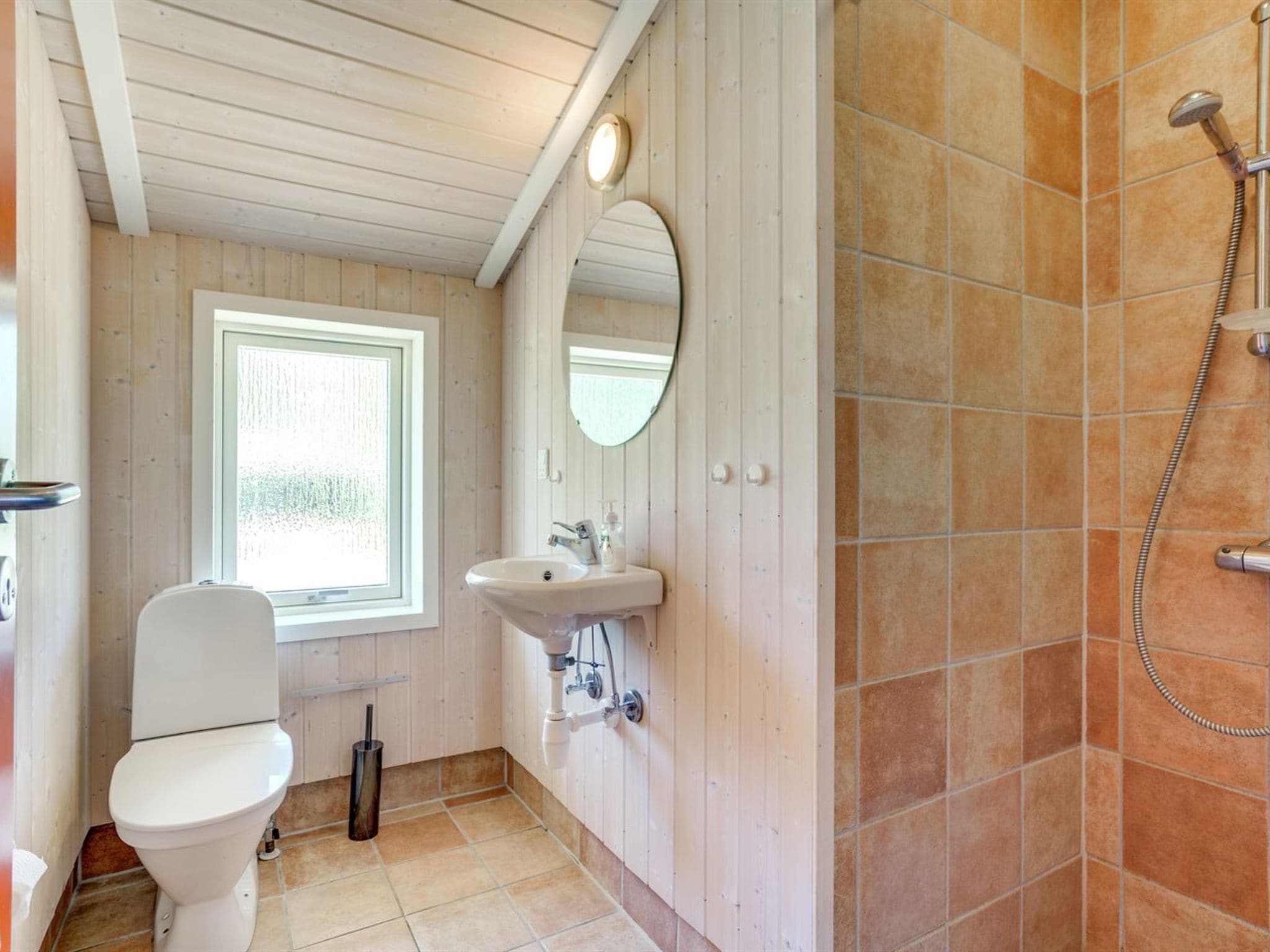 A bathroom with a toilet, sink, mirror, and shower.