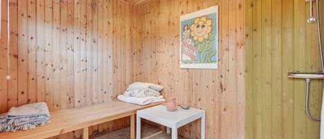 A wooden room with a bench, a small table, and a shower area.