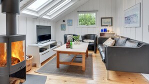 Ein modernes Wohnzimmer mit Kaminofen, Flachbildfernseher, einer Couch und einem Esstisch.