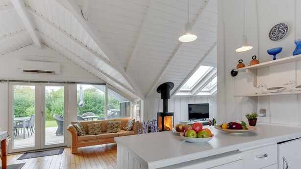 Eine moderne Küche mit weißen Schränken, einer zentralen Kochinsel mit Obst, einem eingebauten Herd und einem Essbereich mit einer Couch und einem Tisch.