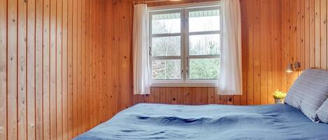 A wooden-paneled room with a bed, a window with curtains, and a hanging light fixture.