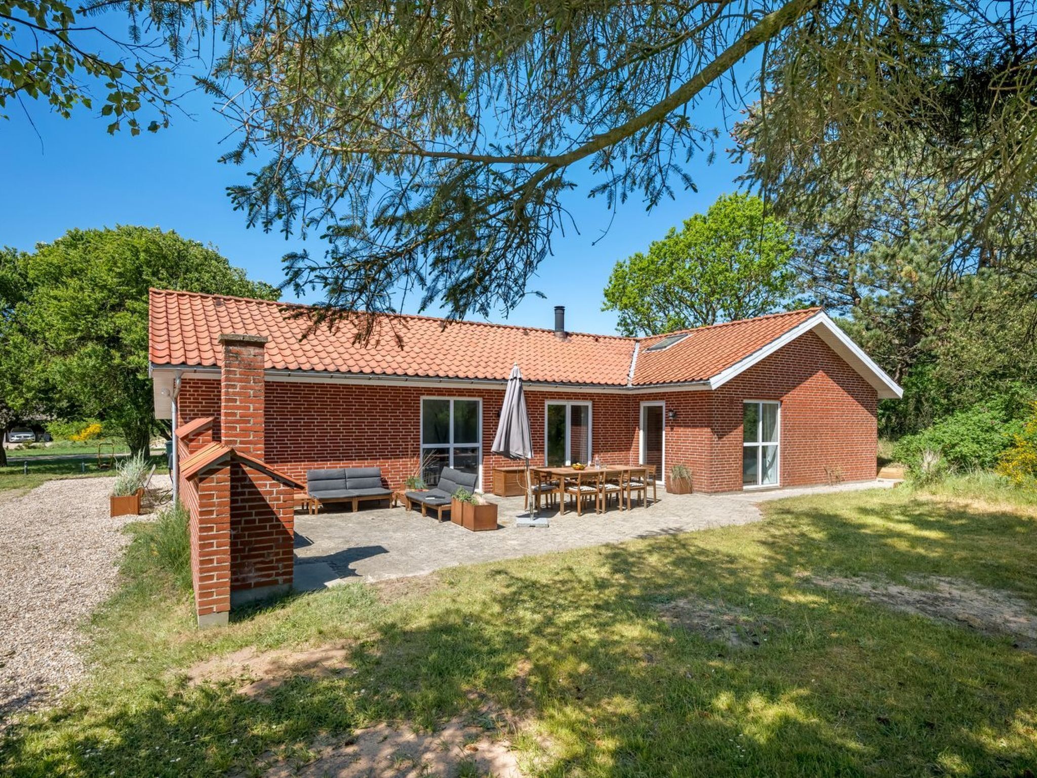 Une maison en briques avec un toit en tuiles, une terrasse avec des meubles d’extérieur et une grande fenêtre.