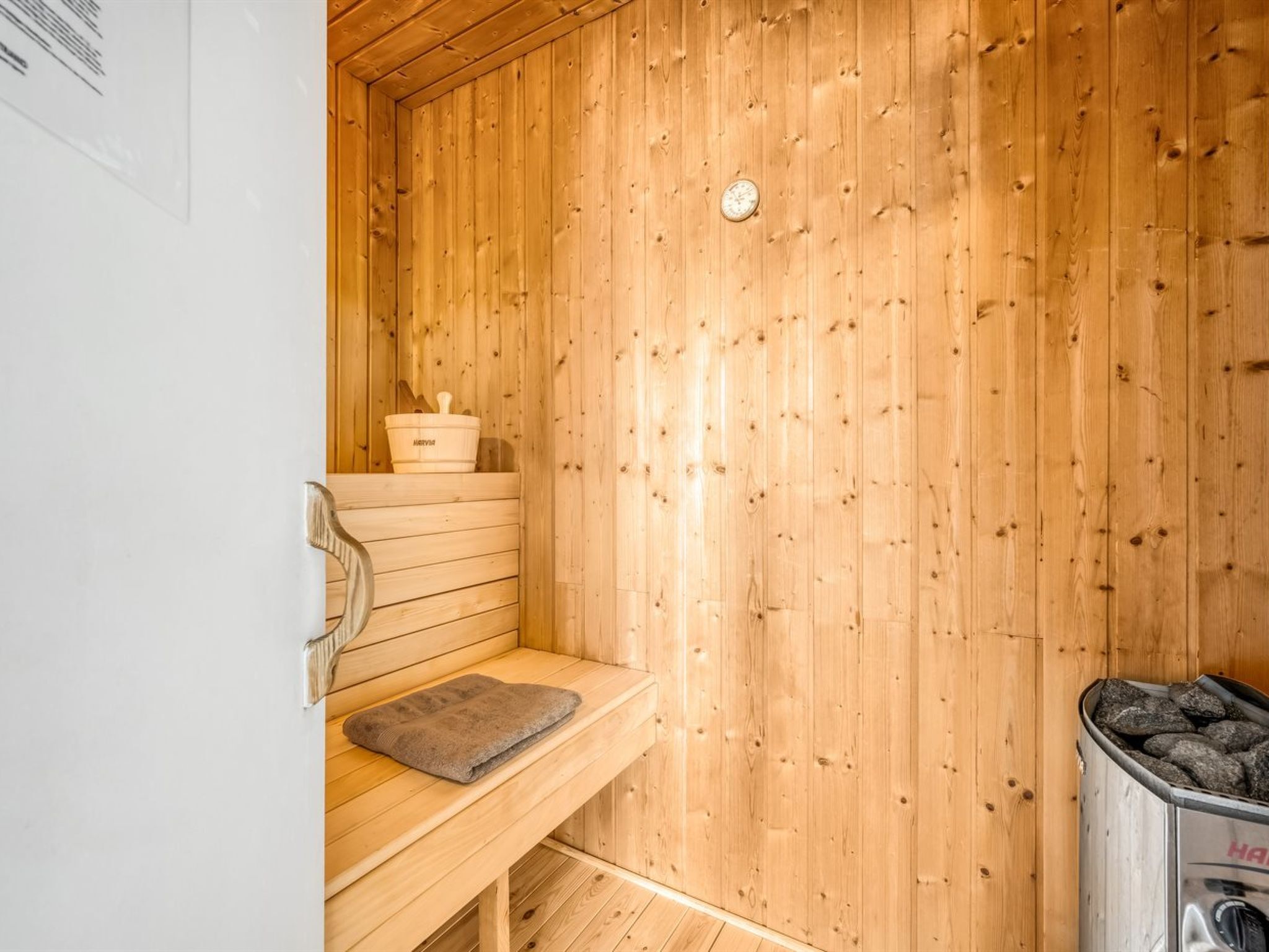 Ein Saunaraum mit Holzwänden, einer Sitzbank, einer Saunahülle und einem Behälter mit Steinen.