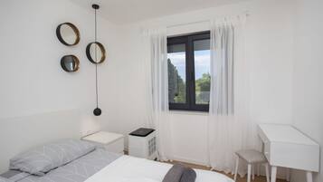 Un dormitorio con cama, escritorio, silla, calefactor y ventana con cortinas.