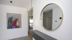 A hallway with a modern art piece on the left, a round mirror on the right, and a grey console. - Mondo Sole in Sveti Bartul (Rasa)