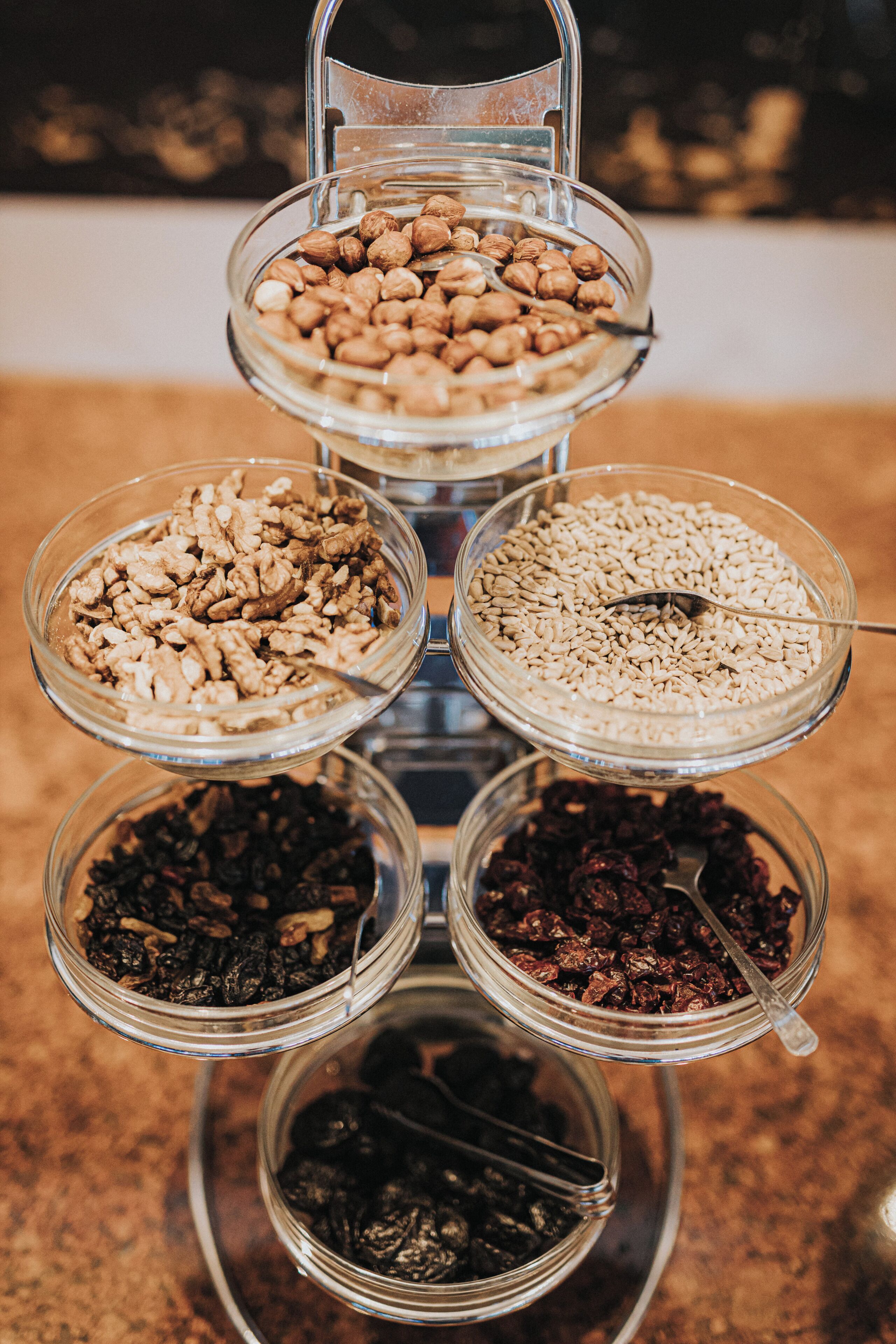 A multi-tiered glass display stand with various nuts and seeds.