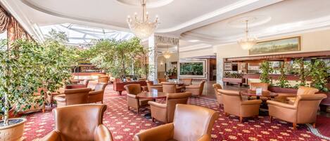 A spacious lobby with leather armchairs, a red patterned carpet, and a chandelier.