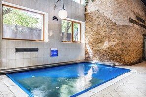 Ein Schwimmbecken mit Fliesenboden, einer Ziegelwand und einem Fenster mit Blick auf einen Baum.