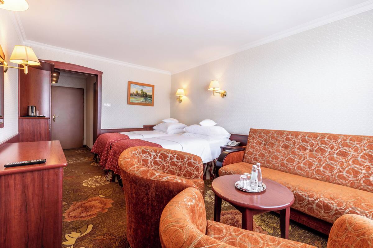 A hotel room with a bed, two sofas, a desk, and a small table.