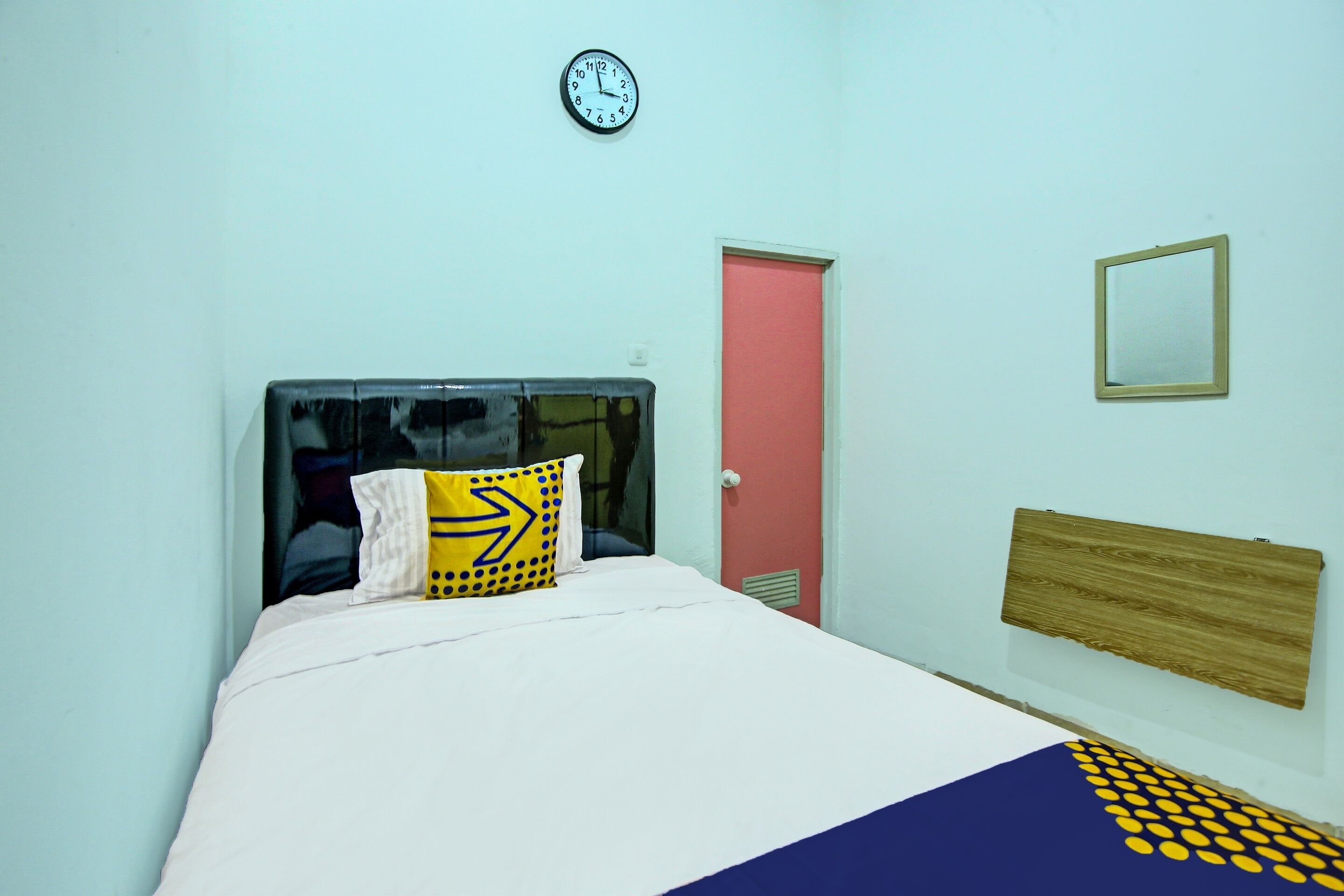 Ein Zimmer mit einem Bett, einer Uhr, einer Tür und einem Spiegel an der Wand.