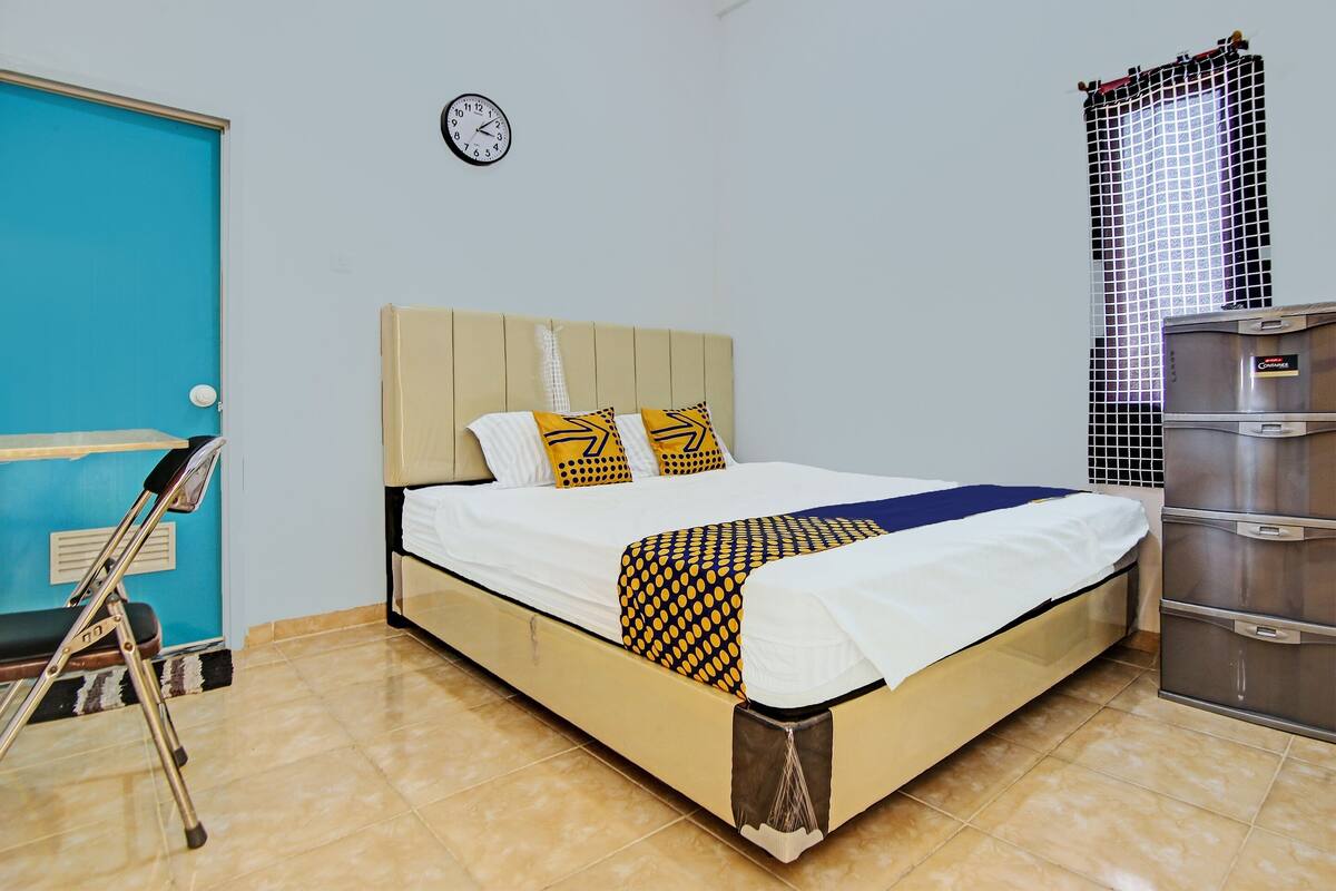 Une pièce avec un lit, une horloge, une porte bleue, une béquille et une armoire en métal.
