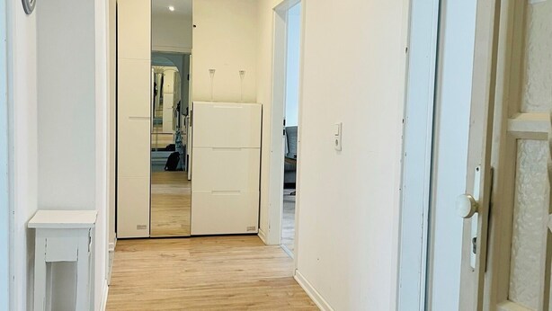 A hallway with wooden flooring, white walls, and a door with a no-smoking sign. - Apartment MARINA (Bremerhaven)