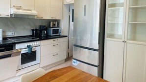 A compact kitchen with white cabinets, a stainless steel refrigerator, a microwave, and a built-in oven. - Apartment MARINA (Bremerhaven)