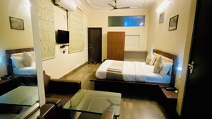 A hotel room with a bed, a desk, a chair, a TV, and a ceiling fan. - Hotel Mock Orange (Jaipur)