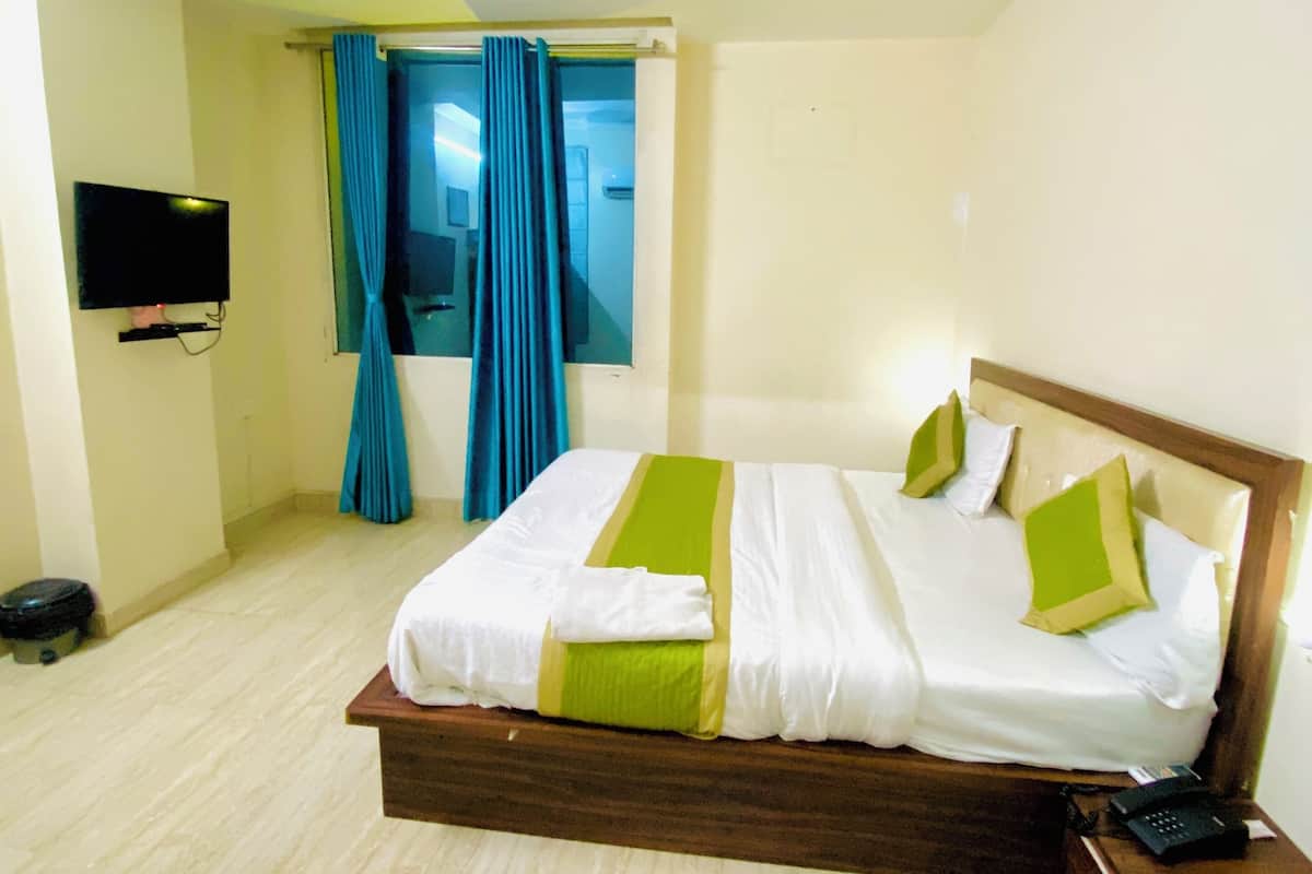A hotel room with a large bed, a TV mounted on the wall, and a window with curtains.