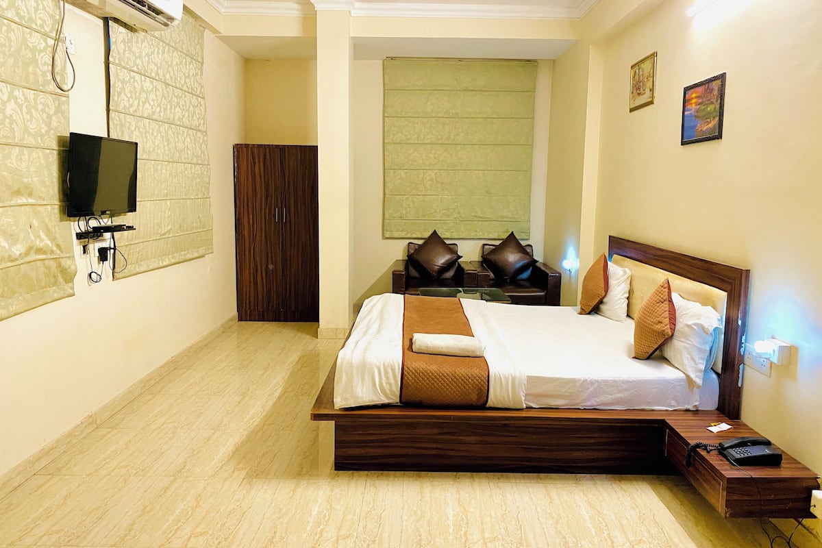 A hotel room with a large bed, a TV mounted on the wall, a desk with a phone, and a window with a view.