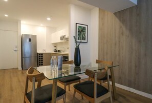 Una cocina moderna con electrodomésticos de acero inoxidable, una zona de comedor con mesa de vidrio y sillas de madera, y una pared decorativa de madera.