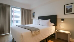 Ett hotellrum med en stor säng, ett nattduksbord, en inramad tavla på väggen och ett fönster med gardiner.