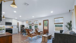 A spacious living room with a dark sofa, two armchairs, a coffee table, and a dining area with a table and chairs. - Ms Dot’s 290 Wine Trail Farmhouse-Downtown- Fire Pit - Covered Patio (Johnson City)